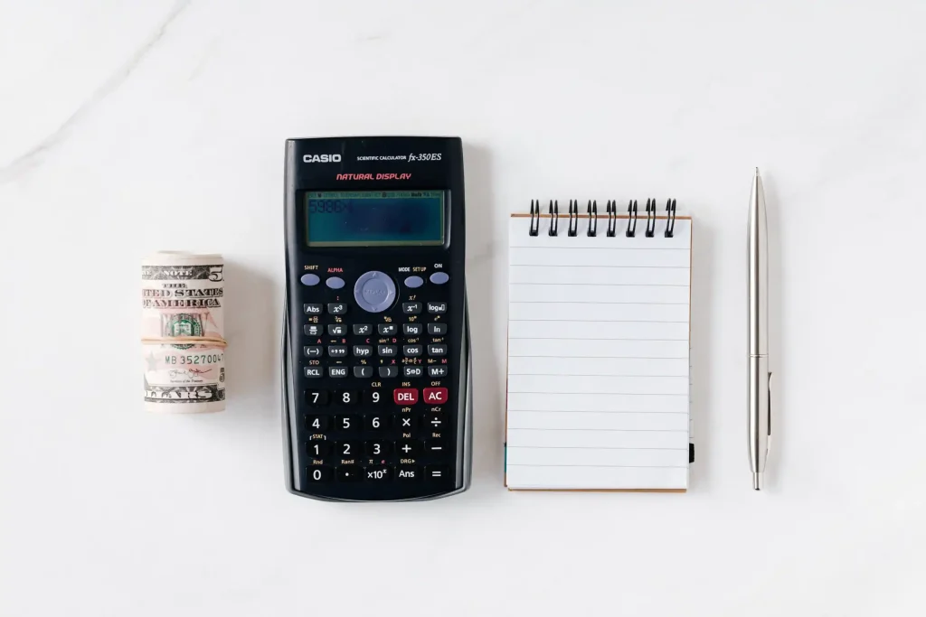 Calculator and rolled cash next to a notepad and pen, symbolizing financial calculations and stock donation processes for nonprofits.